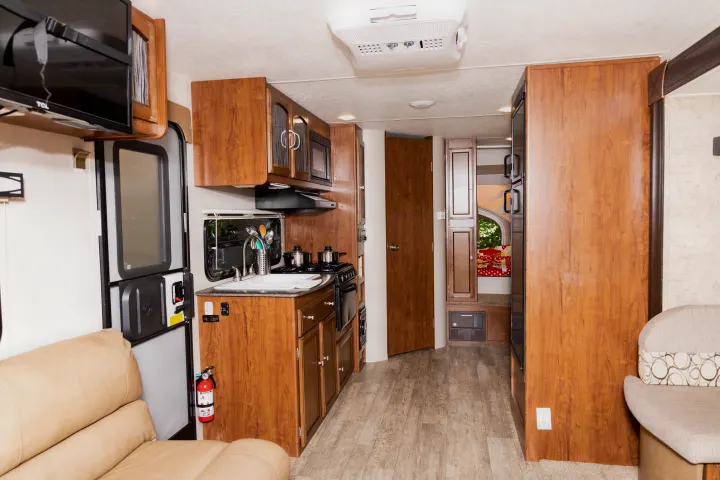 Inside this comfy **rv rental**: a kitchen with sink, stove, microwave, and cabinets, plus a sofa and wood-look flooring.. Coachmen Freedom Express 2018