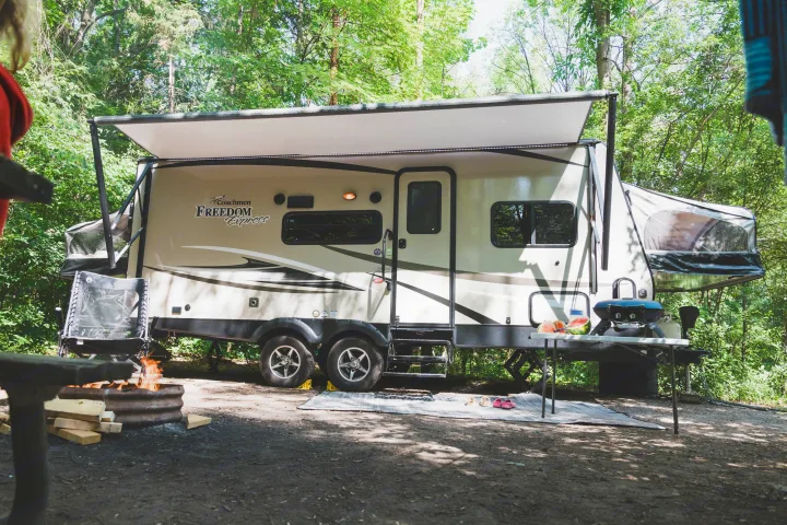 An RV rental parked at a serene campsite, featuring an extended awning, ready for outdoor cooking and a cozy campfire.. Coachmen Freedom Express 2018