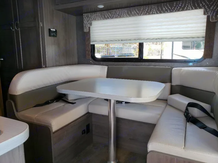 Comfortable U-shaped dinette and table inside an RV rental. Features two-tone seating, window, and wall controls.. Winnebago Minnie Winnie 2017