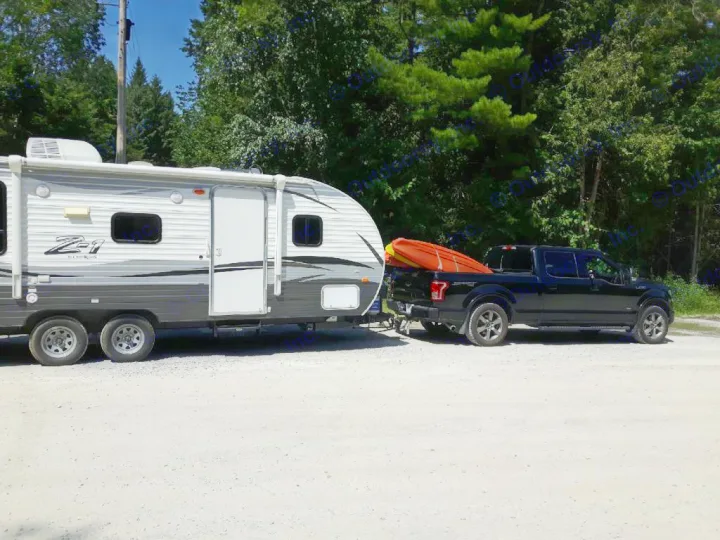 A black pickup truck with a kayak tows an RV rental (travel trailer) on a gravel road, ready for adventure.. Crossroads Z-1 2017