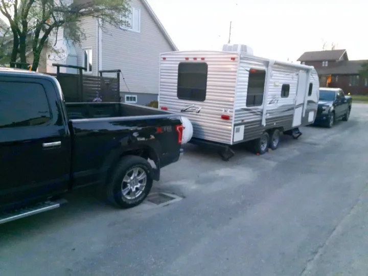 Black pickup truck towing an RV rental on a residential street, with another truck behind it.. Crossroads Z-1 2017