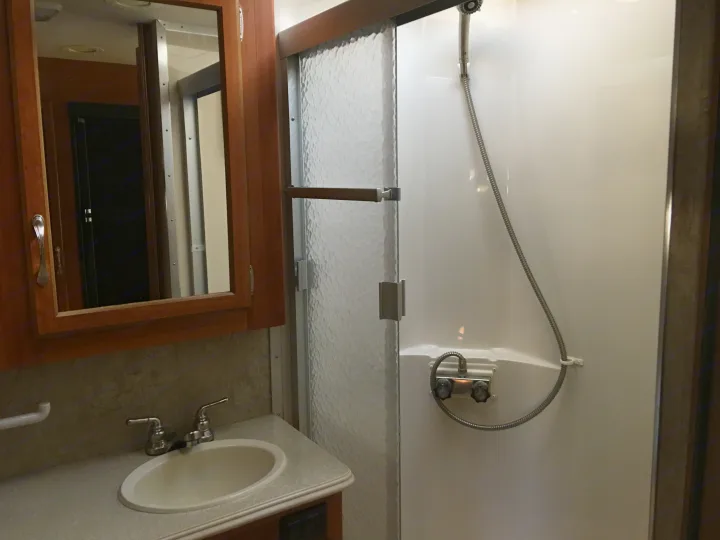 Compact RV rental bathroom featuring a vanity, sink, mirrored cabinet, and a shower with a handheld showerhead.. National Surf Side 2006