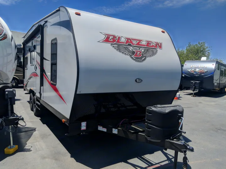 Front view of a white Blazen travel trailer RV rental with black and red graphics, parked in an outdoor lot on a sunny day.. Pacific Coachworks Blaze'N 2019