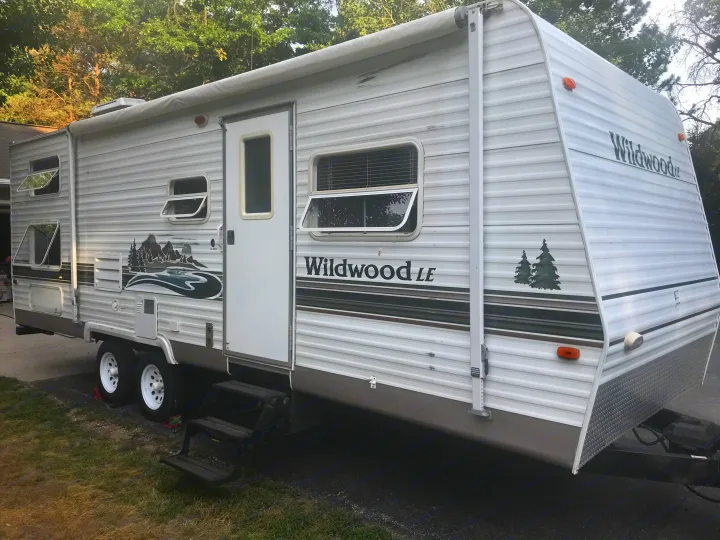 Side view of a white Wildwood travel trailer RV, ideal for an rv rental. Shows windows, door, awning, and decorative graphics.. Forest River Wildwood 2005
