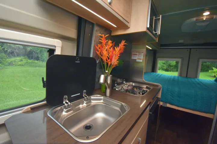 This RV rental offers a cozy interior, featuring a compact kitchen with a sink, stove, and a comfortable bed.. Hymer Aktiv 2018