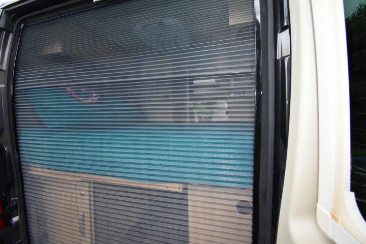 Pleated privacy screen on an RV rental door, partially obscuring the interior bed, fan, and cabinets.. Hymer Aktiv 2018