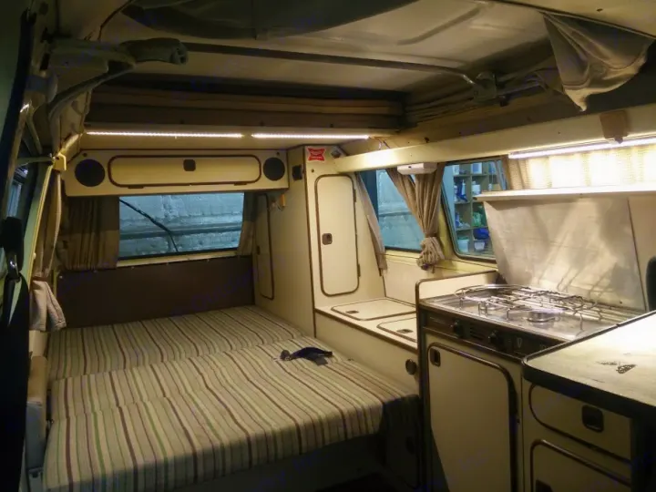 Explore this inviting RV rental campervan interior featuring a comfortable bed, compact kitchen, and overhead storage.. Volkswagen Westfalia 1982