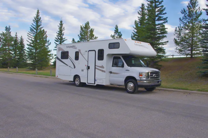 White Majestic Class C rv rental motorhome parked on an asphalt road beside pine trees under a cloudy sky, ready for travel.. Other Other 2012
