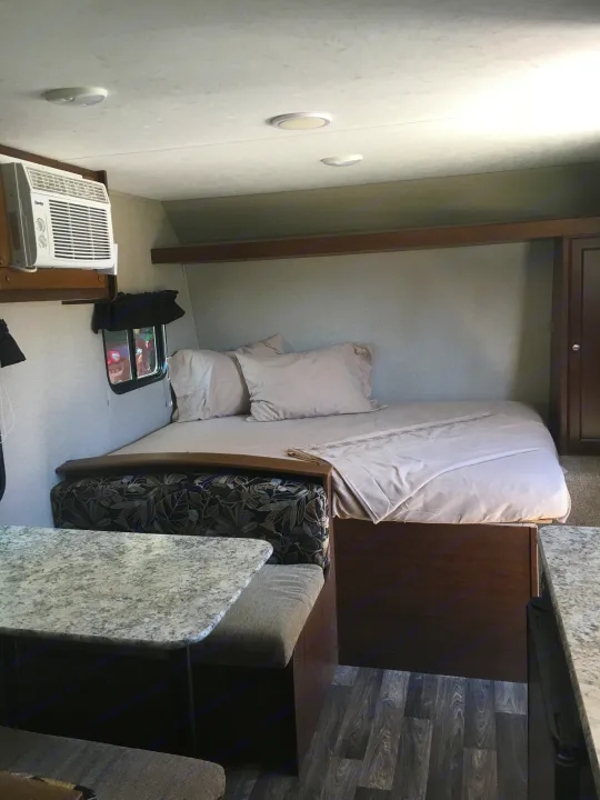 Cozy RV rental interior featuring a bed, dining nook, and AC unit. Compact and functional space.. Keystone Hideout 2017