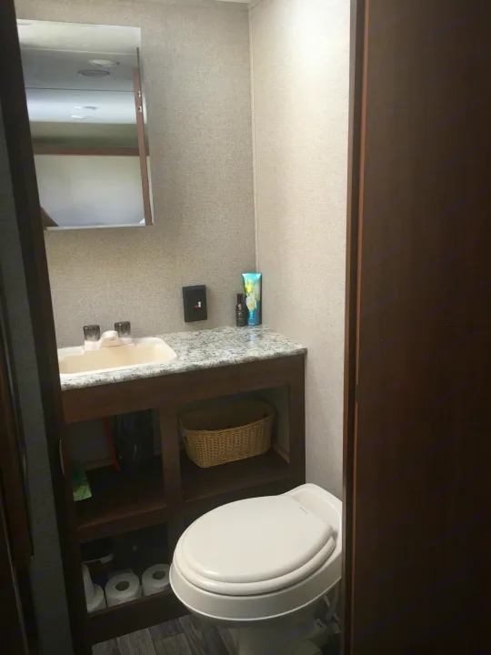 A well-equipped RV rental bathroom features a sink, toilet, mirror, and accessible under-sink storage.. Keystone Hideout 2017