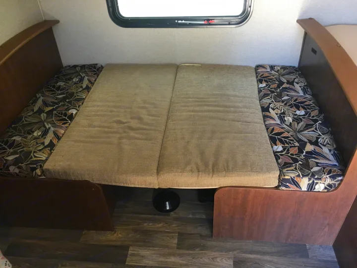 RV rental interior: A dinette converted to a sleeping area with patterned and solid beige cushions, seen below a window.. Keystone Hideout 2017