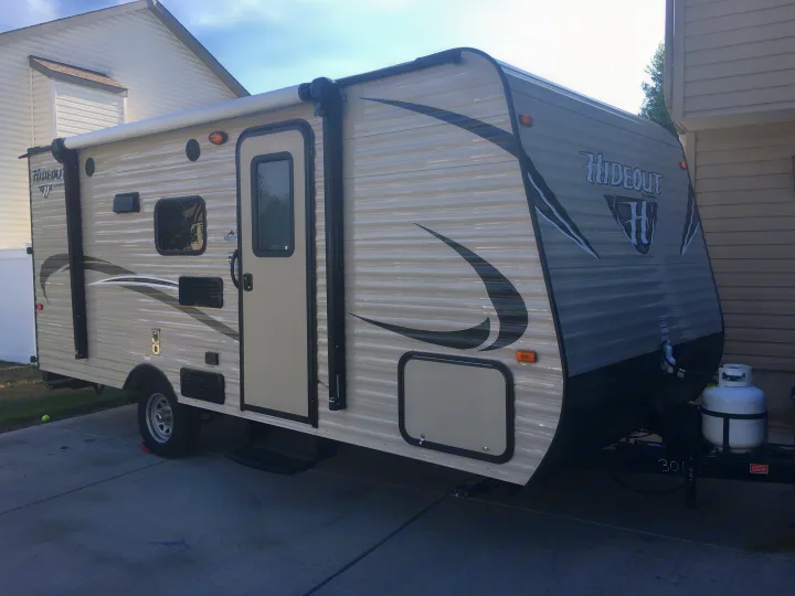 A light-colored Hideout travel trailer, resembling an rv rental, is shown parked on a driveway. An awning is visible on its side.. Keystone Hideout 2017