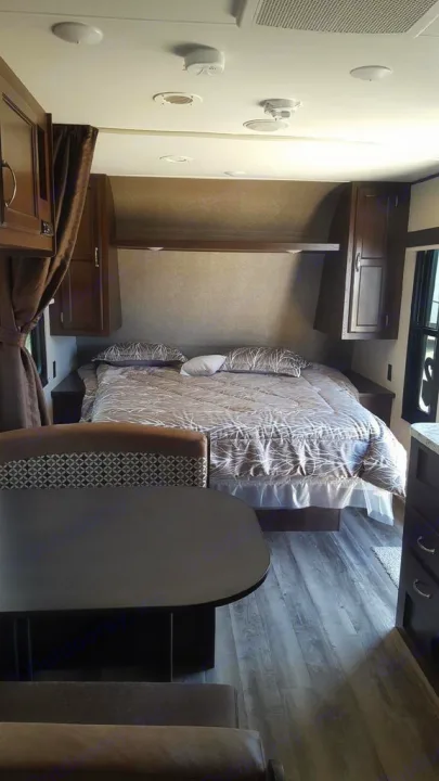 RV rental interior showing a comfortable bedroom with patterned bedding and overhead cabinets, adjacent to a cozy dining area.. Jayco Jay Flight 2018