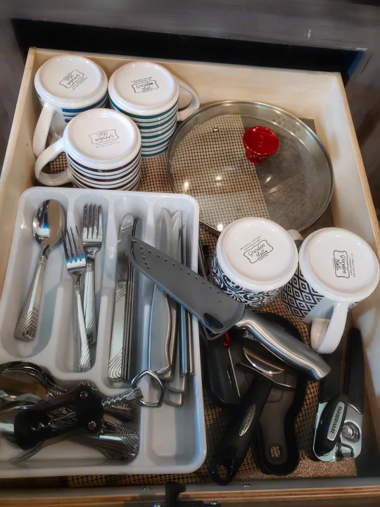 Organized RV rental kitchen drawer with Graydon Hall mugs, silverware, a pot lid, and Farberware tools.. Winnebago Minnie Winnie 2017