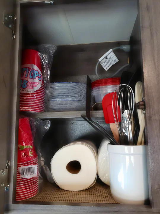 Organized RV rental kitchen cabinet: disposable cups, plates, paper towels, and utensils on non-slip liners.. Winnebago Minnie Winnie 2017