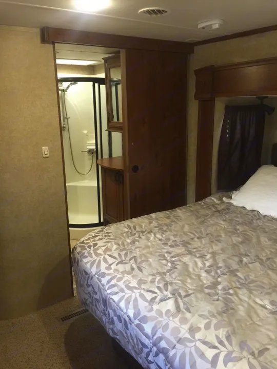 Cozy RV rental bedroom with patterned comforter; compact bathroom with shower stall visible through a sliding door.. Open Range 427 BHS 2014