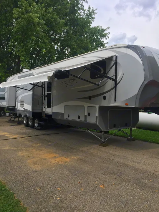 This grey and white fifth-wheel RV rental, an Open Range model, is parked on an asphalt lot, ready for camping trips.. Open Range 427 BHS 2014