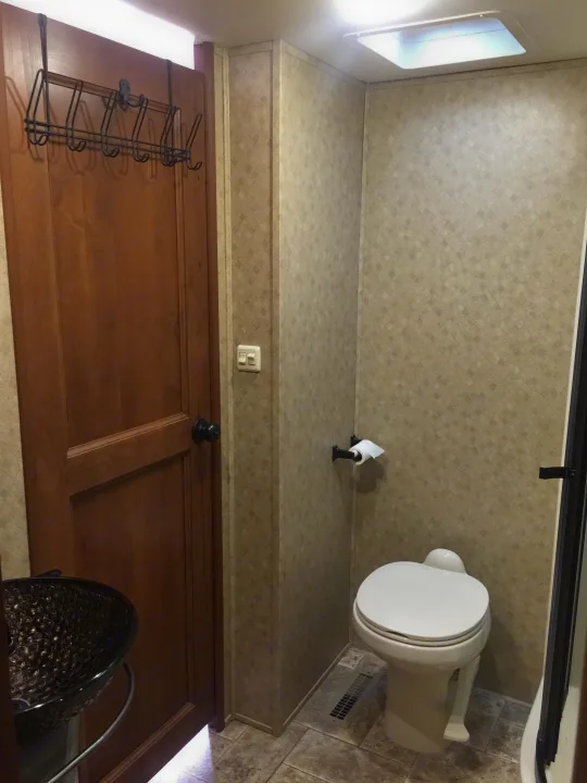 This RV rental bathroom features a white toilet, toilet paper holder, a floor vent, and a wooden door with an over-the-door hook rack.. Open Range 427 BHS 2014