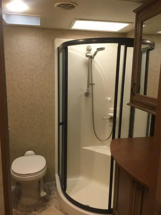 Compact RV rental bathroom, featuring a toilet, corner shower with glass door, and wooden vanity with mirror.. Open Range 427 BHS 2014