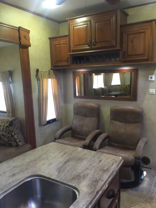 Detailed view of a cozy RV rental living area with kitchen sink, two brown recliners, and wooden cabinetry.. Open Range 427 BHS 2014