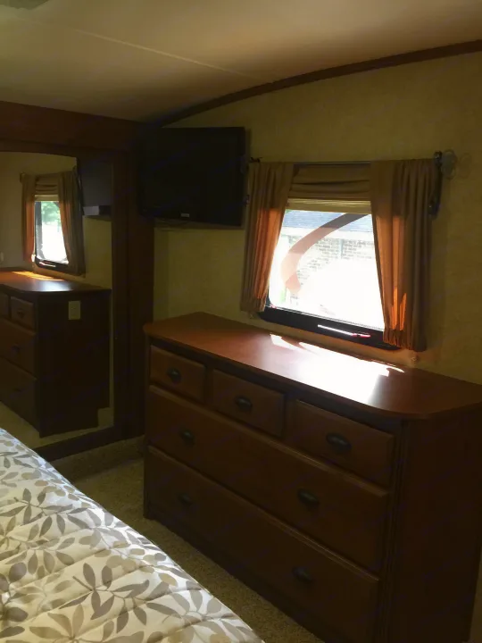 RV rental bedroom: wooden dresser, wall-mounted TV, bright window, and patterned bed. Mirrored storage seen left.. Open Range 427 BHS 2014