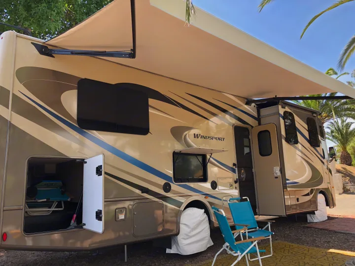 Relaxing by an RV rental with the awning extended at a sunny campsite. Ready for your next outdoor adventure!. Thor Windsport 2018