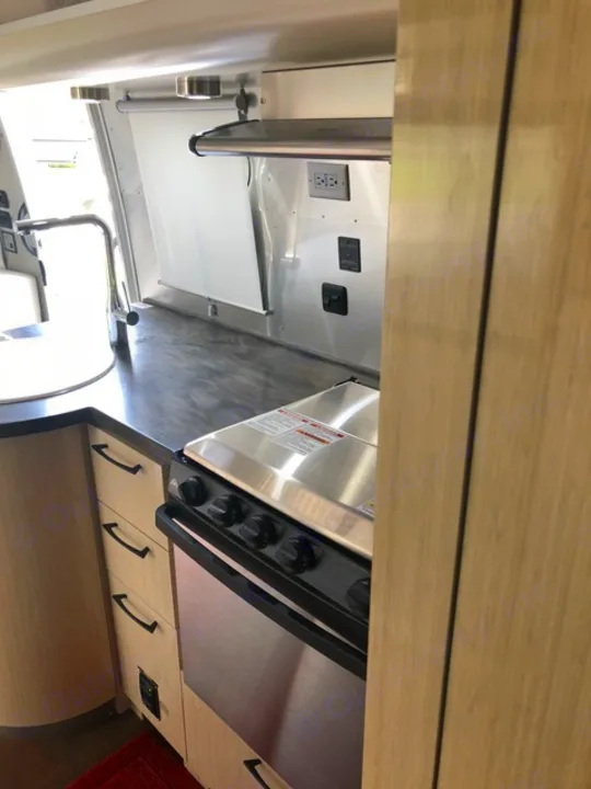 RV rental kitchen interior: stainless steel stove, sink, and wood cabinets with power outlets visible.. Airstream Flying Cloud 2017