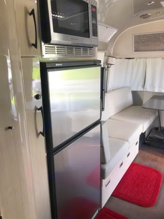 Explore this RV rental's modern interior: a sleek kitchen with microwave & Dometic fridges, plus comfy white seating.. Airstream Flying Cloud 2017