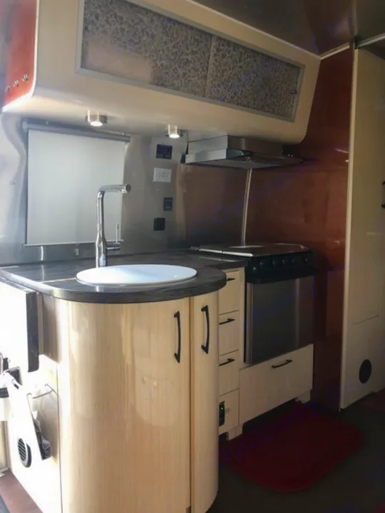 Interior view of an RV rental kitchen with modern light wood cabinets, sink, stove, and counter space.. Airstream Flying Cloud 2017