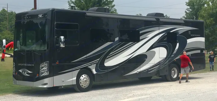 Sportscoach RV rental: A large black motorhome with sleek graphics, parked on a gravel lot with people nearby.. Coachmen Sportscoach 2018