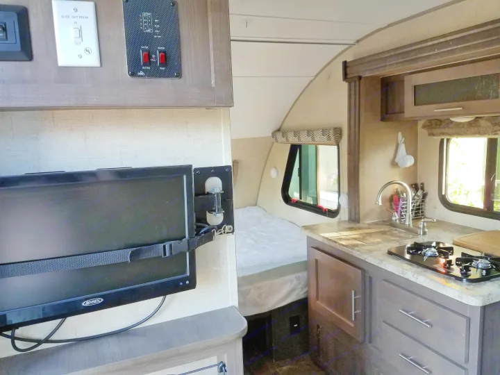 This rv rental's interior features a TV, a cozy bed, compact kitchen with sink and stove, and control panels.. Forest River R-Pod 2016
