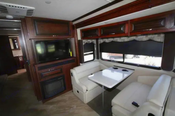 Spacious RV rental interior with white dinette, entertainment unit, and electric fireplace. Comfort on the road.. Holiday Rambler Vacationer 2017