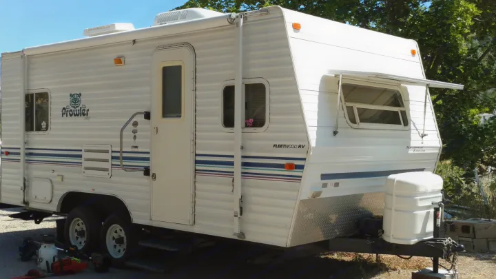 White Fleetwood Prowler travel trailer, great for RV rental. Shows side view, awning, windows, and front hitch area.. Fleetwood Prowler 2002