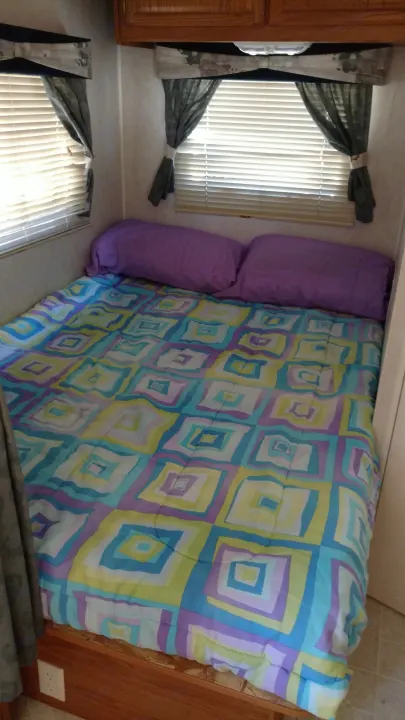 Cozy RV rental bedroom with a colorful geometric comforter, purple pillows, and bright windows with blinds.. Fleetwood Prowler 2002