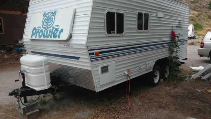 Front-side view of a white Prowler travel trailer, ready for your next rv rental adventure. Shows propane tanks & power hookup.. Fleetwood Prowler 2002