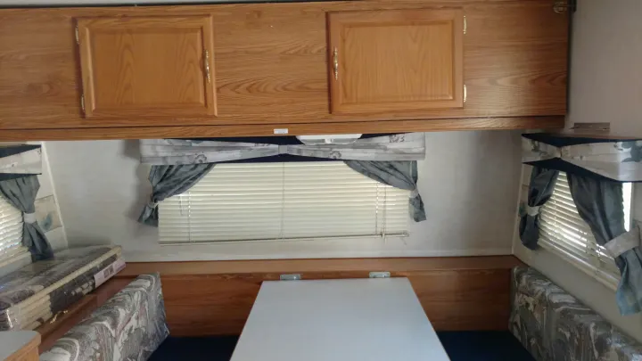 RV rental dinette area: wood cabinets, patterned seating, window blinds, and new bedding visible on the left.. Fleetwood Prowler 2002