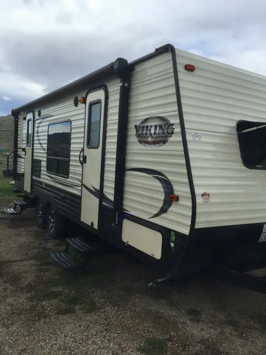 This modern Viking travel trailer, ideal for an RV rental, is shown with its light-colored exterior, windows, and retracted awning.. Forest River Viking 2018