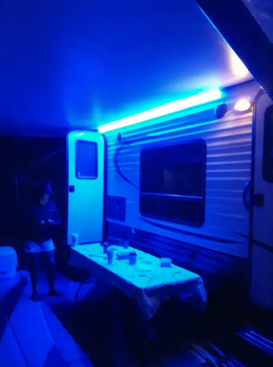 This RV rental's awning area is lit by vibrant blue LEDs at night, showcasing a person and a table, perfect for camping evenings.. Forest River Viking 2018
