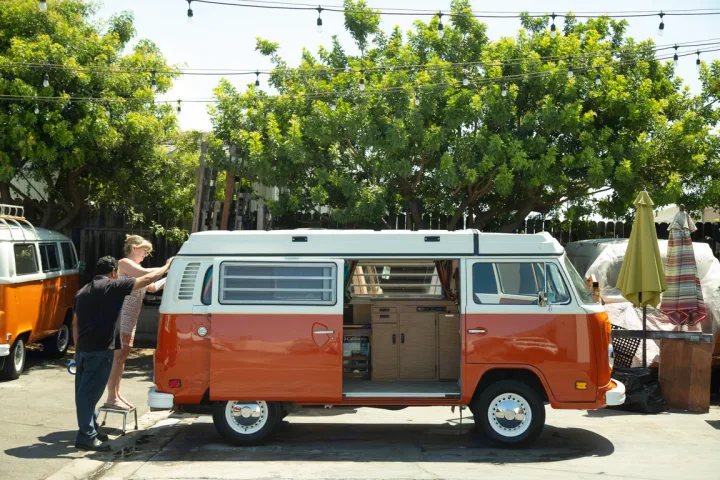 Prepping a classic orange and white VW camper RV rental. A couple gets ready for adventure in their retro travel van.. Volkswagen westfalia 1979