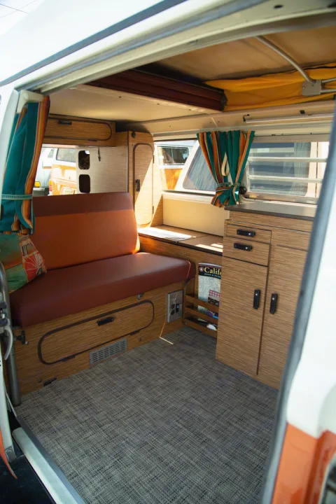 Explore this RV rental! Inviting camper van interior with orange seating, wood cabinetry, patterned floor & striped curtains.. Volkswagen westfalia 1979