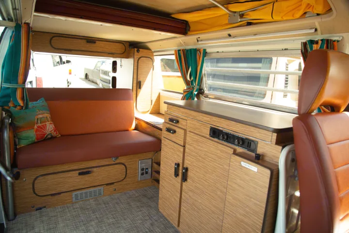 Interior of a vintage camper van, perfect for RV rental adventures, featuring cozy seating, wood cabinets, and a pop-top.. Volkswagen westfalia 1979