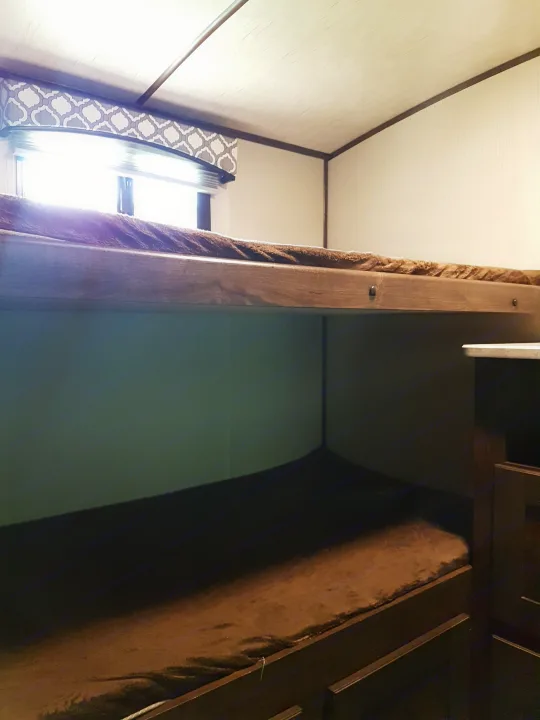 Compact RV rental interior featuring a bright window with patterned curtains, a wooden bunk frame, and light-colored walls.. Cruiser Rv Corp Radiance 2019