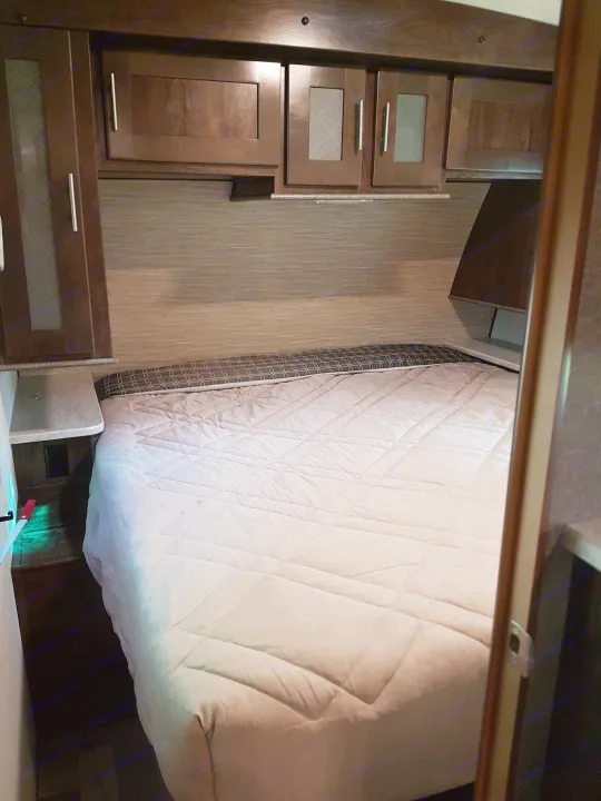 RV rental interior: bedroom with dark cabinets, a quilted bed, and a mattress with highlighted spots, possibly stains, under light.. Cruiser Rv Corp Radiance 2019