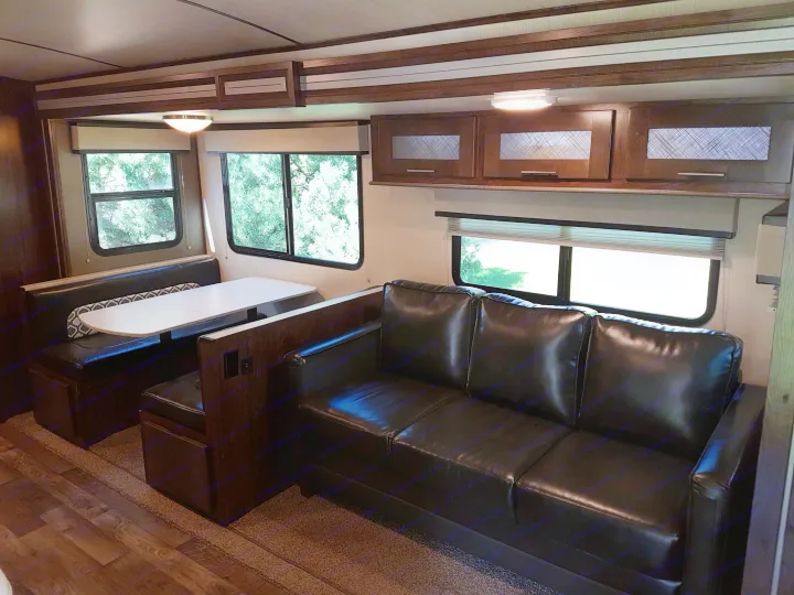 Spacious RV rental interior with comfy seating, modern wood cabinetry, and large windows showing lush greenery.. Cruiser Rv Corp Radiance 2019