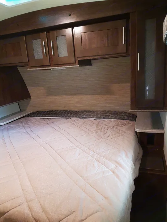 Cozy RV rental bedroom featuring dark wood cabinets, a comfy quilted bed, and patterned curtains.. Cruiser Rv Corp Radiance 2019