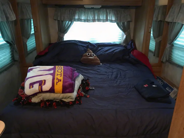 Cozy RV rental bedroom with dark blue bedding, a novelty poop emoji pillow, and purple Minnesota blankets.. Gulf Stream Sun Stream 1995