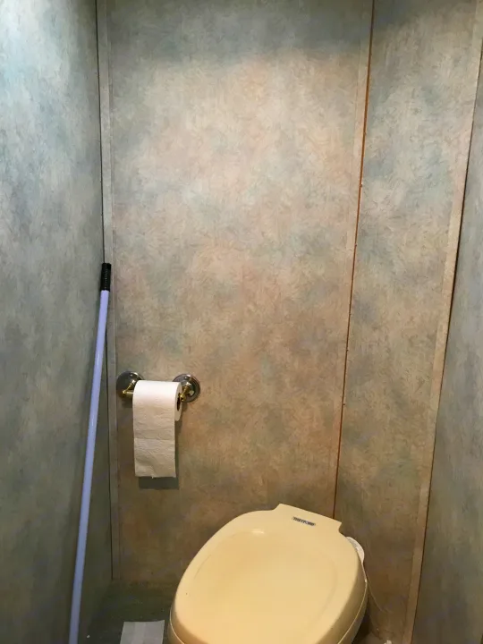 Inside an RV rental, a compact bathroom features a Thetford toilet, toilet paper holder, and a white pole leaning by the wall.. Gulf Stream Sun Stream 1995