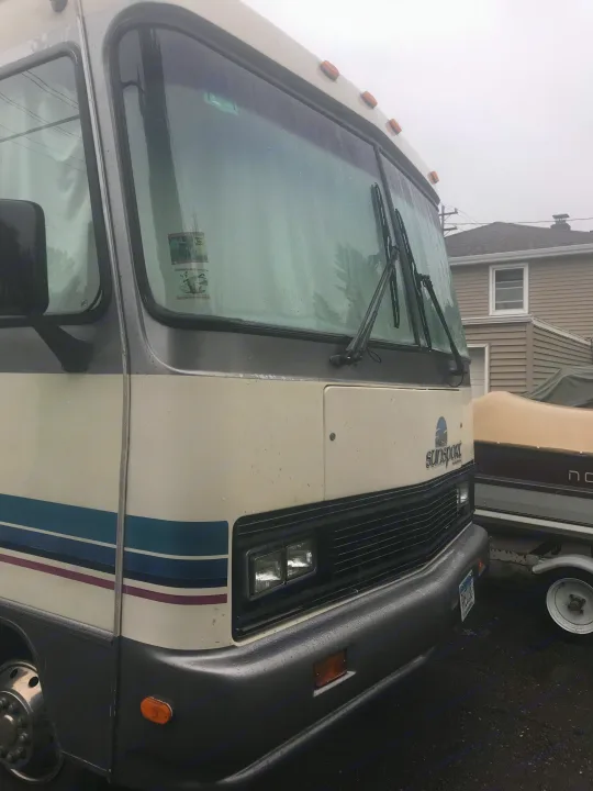Front of a parked white and grey Sunsport RV rental on a damp day. Visible features: headlights, wipers, and the Sunsport logo.. Gulf Stream Sun Stream 1995