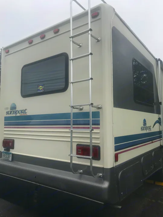 Rear and side of a Sun Sport RV rental: features a ladder, windows, storage, and white body with blue/purple stripes.. Gulf Stream Sun Stream 1995