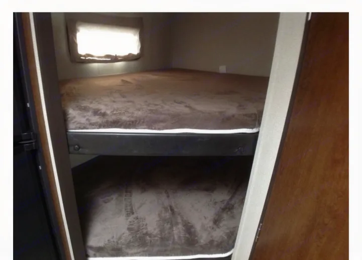 Inside an RV rental, a compact sleeping area features two bunk beds with brown bedding and a window.. Forest River Tracer 2019